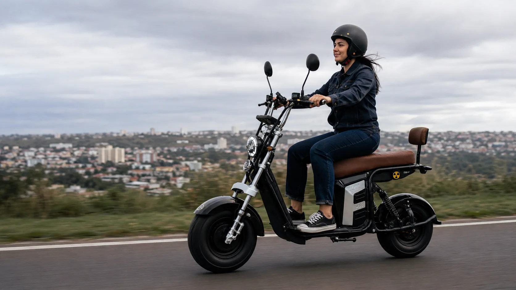 Mulher pilotando a VYA Hard+ em estrada aberta com a cidade ao fundo